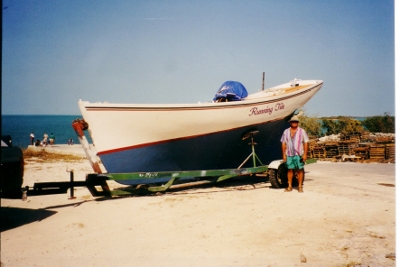 brian stands
            by a Bahamian Fishing Boat on a beach on Long Island